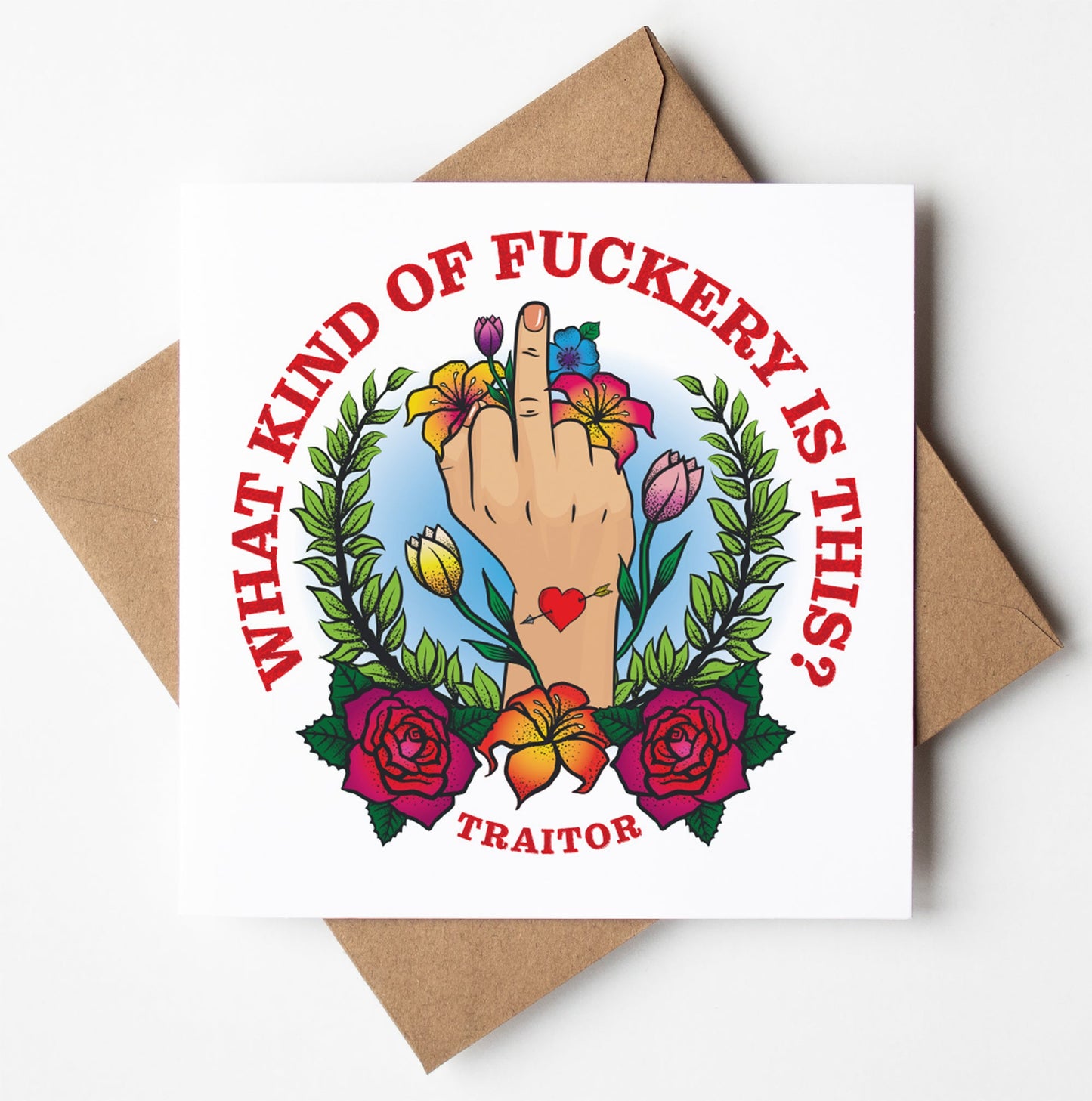 The What Kind Of Fuckery Tattoo Card features a colorful floral illustration with a hand raising the middle finger on a brown envelope. Red text reads, "WHAT KIND OF F**KERY IS THIS?" and "TRAITOR" at the bottom. Enjoy worldwide shipping for this cheeky delight!.