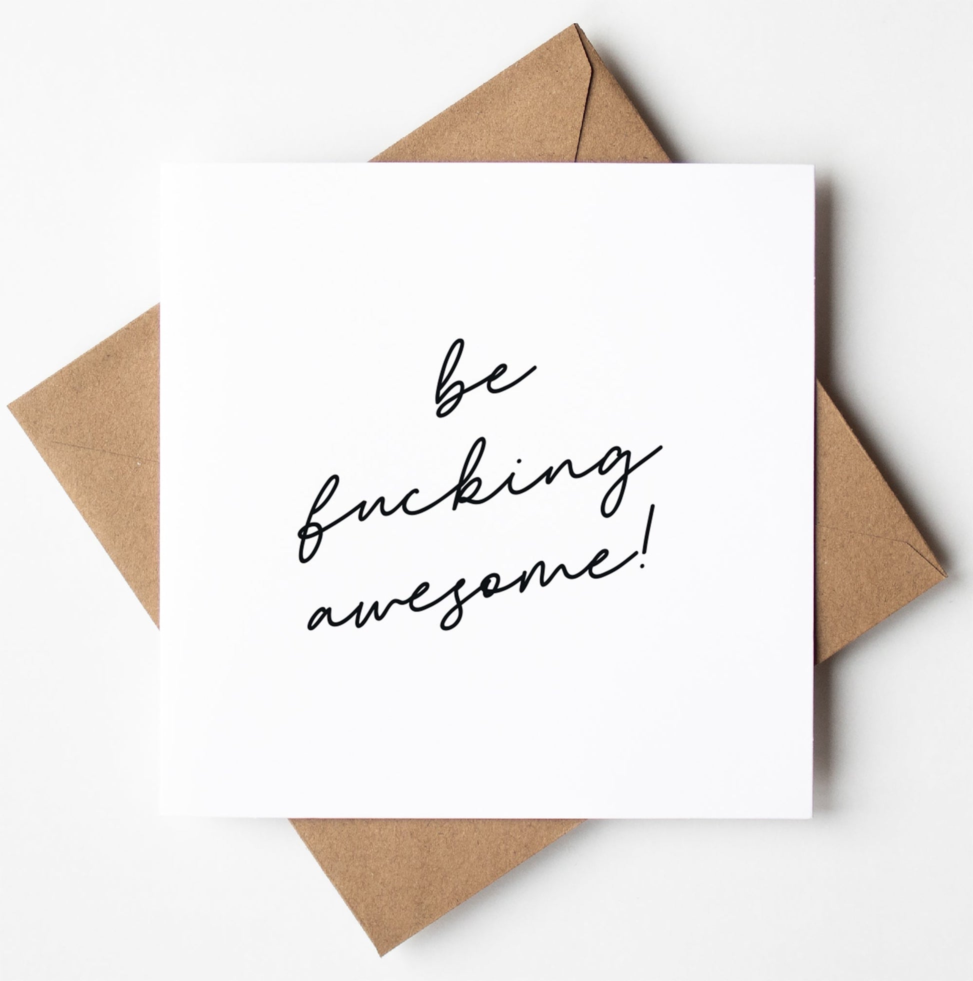 A white greetings leaving card with the handwritten message "be fucking awesome!" placed on a brown envelope, perfect for saying goodbye with good luck vibes.