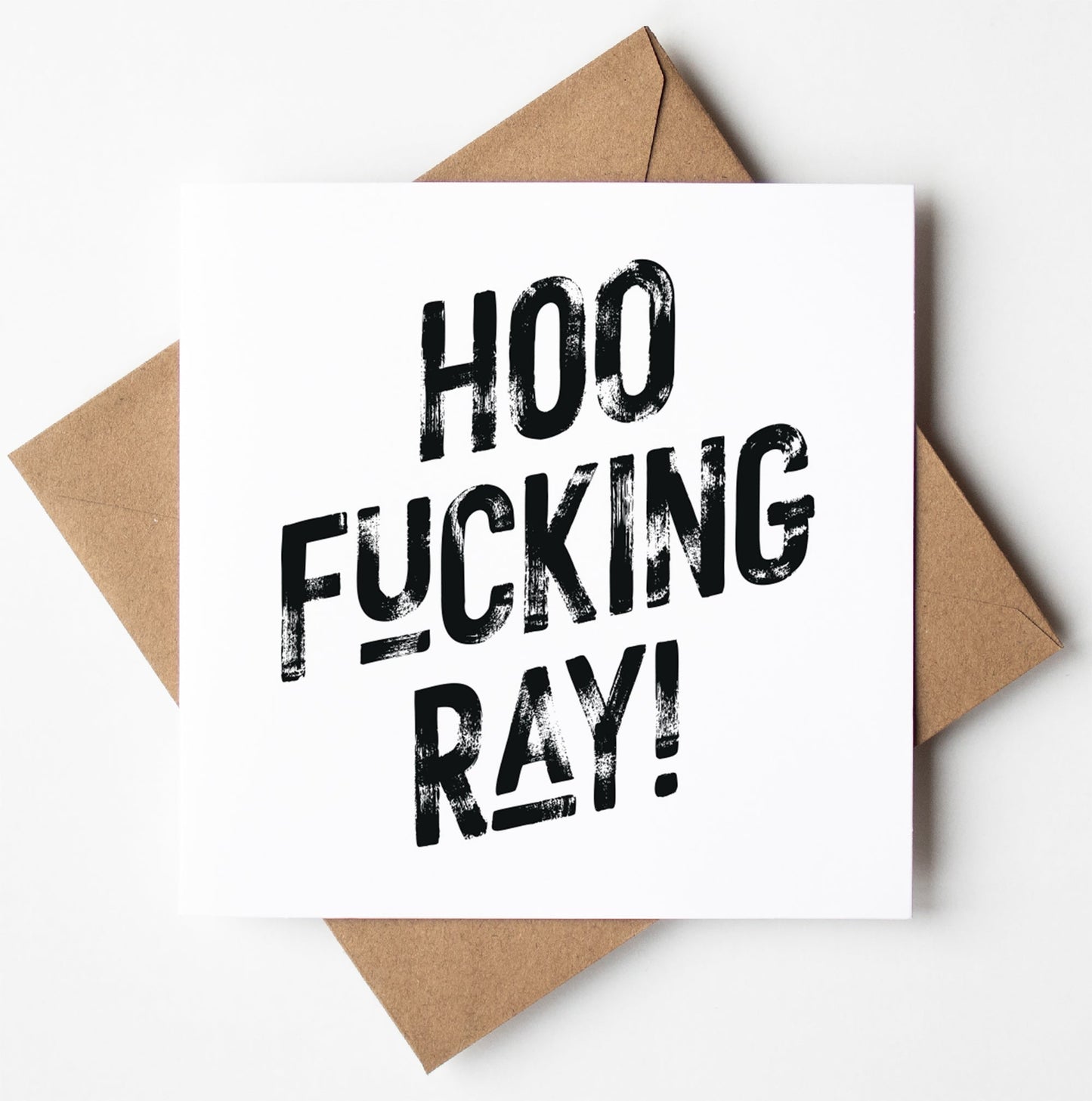 The Hoo Fucking Ray! Harlem Card, a white card featuring bold black text that reads "HOO FUCKING RAY!", is set on a brown envelope, making it an ideal sweary congratulations card. It comes packaged in a biodegradable bag for eco-friendly delivery and offers worldwide shipping.
