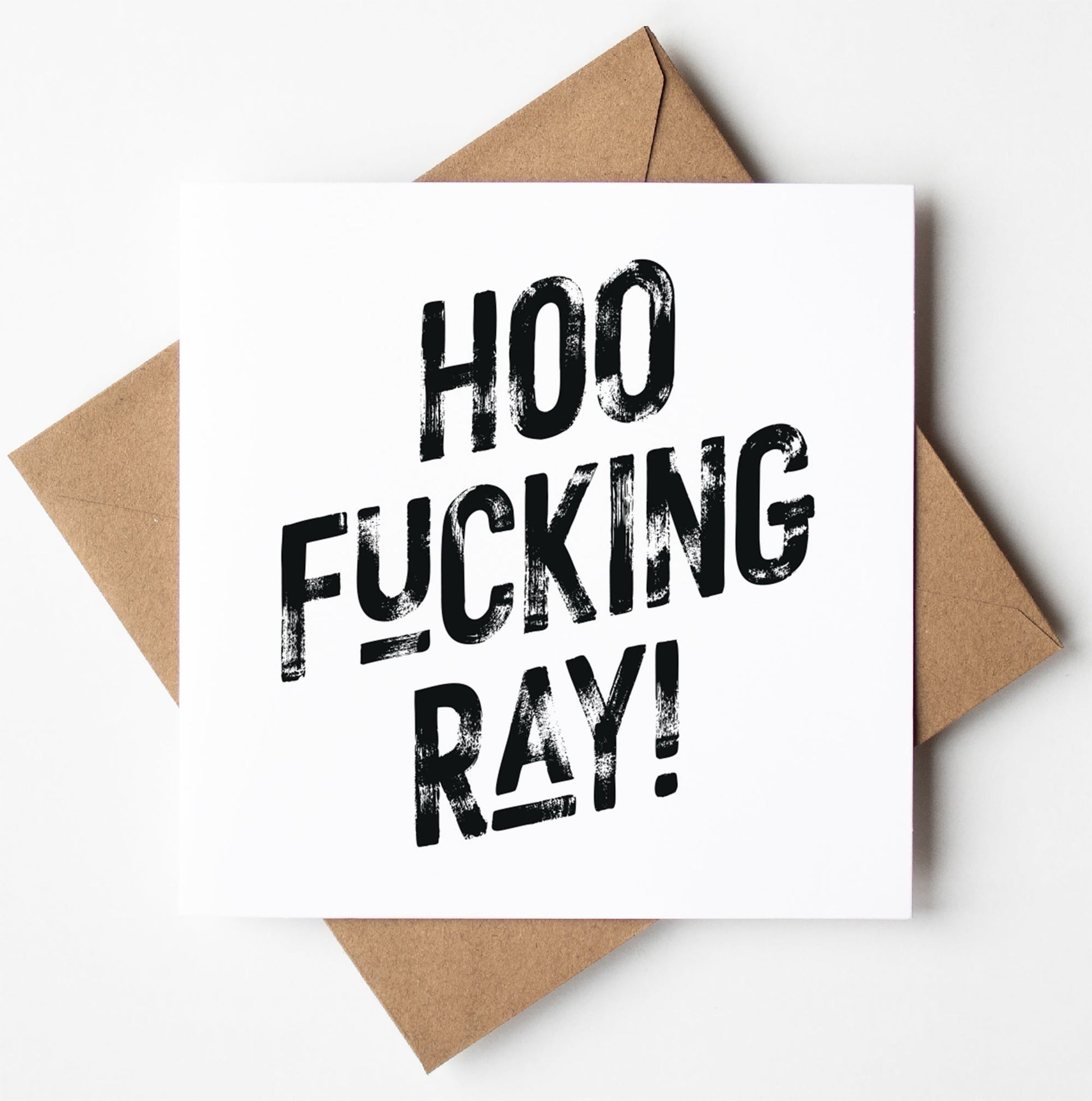 The Hoo Fucking Ray! Harlem Card, a white card featuring bold black text that reads "HOO FUCKING RAY!", is set on a brown envelope, making it an ideal sweary congratulations card. It comes packaged in a biodegradable bag for eco-friendly delivery and offers worldwide shipping.