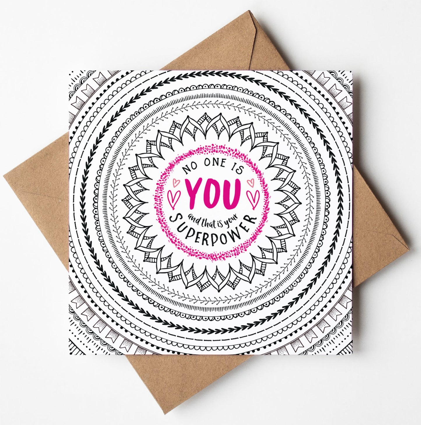 The "No One Is You Card" features an inspiring black and white mandala design with the empowering message "No one is you, and that is your superpower" highlighted in bright pink. This uplifting card is beautifully presented on a brown envelope against a clean white backdrop.