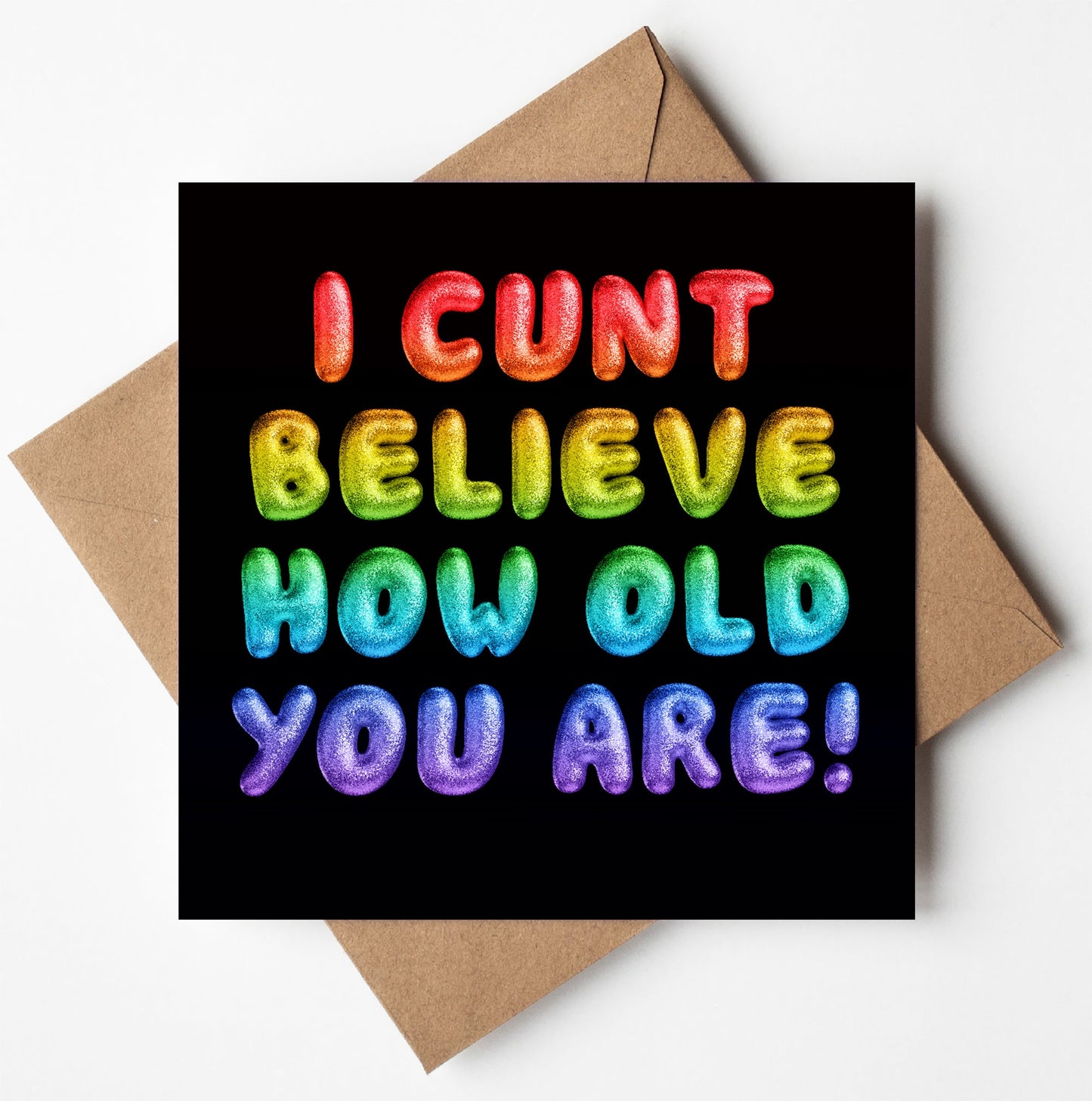 A brown envelope contains the "I Cunt Believe How Old You Are! Rainbow Font Card," featuring colorful, bold, stylized letters against a black background that exclaims, "I CUNT BELIEVE HOW OLD YOU ARE!
