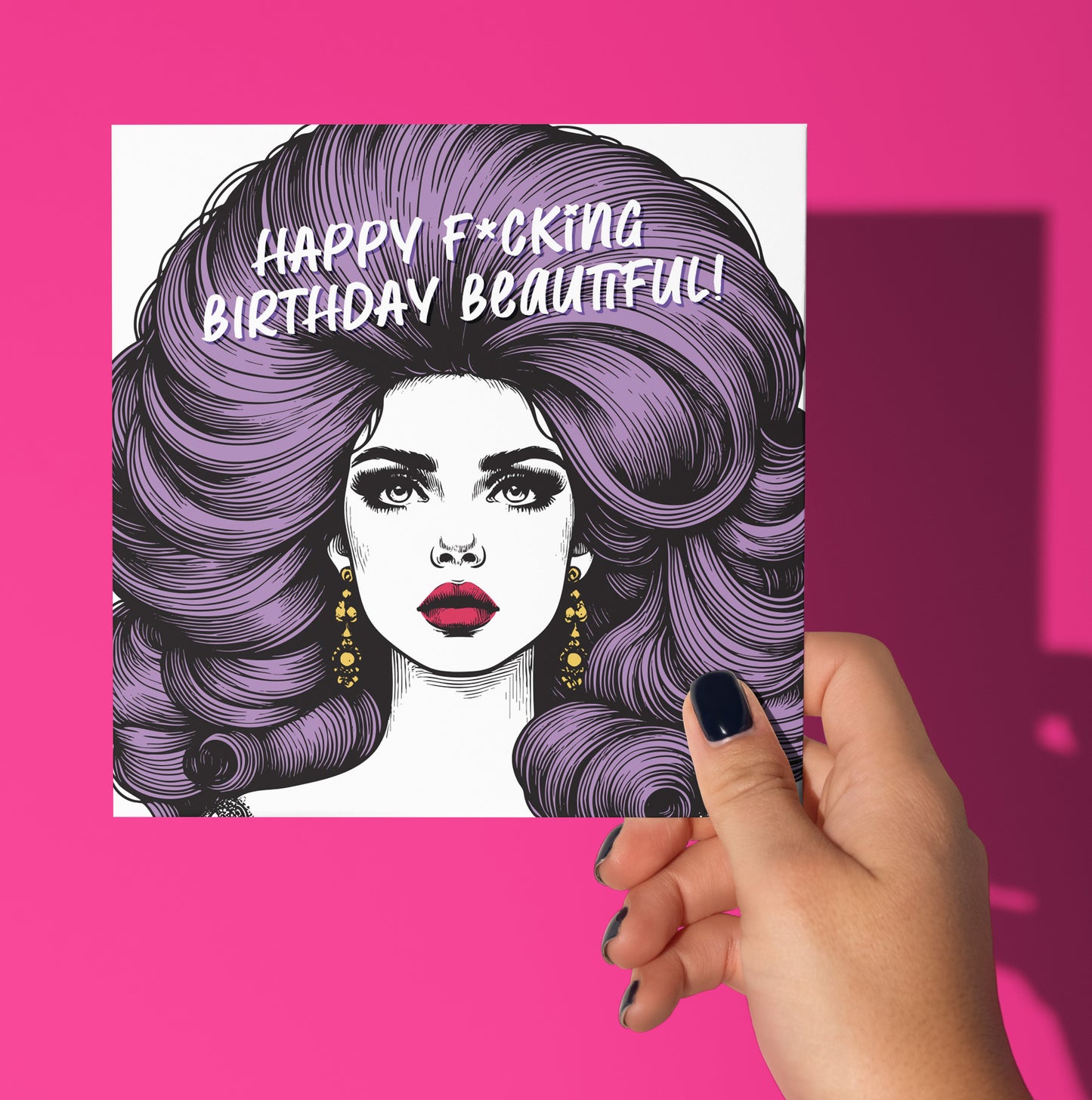 A hand with dark nail polish holds the "Happy F*cking Birthday Beautiful! Vintage Babes Birthday Card," featuring an illustrated woman with big purple hair, gold earrings, and bold makeup on a pink background.