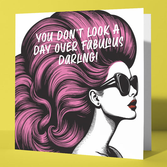 The "You Don't Look A Day Over Fabulous Darling! Vintage Babes Happy Birthday Card" features a chic illustrated woman with pink hair, bold sunglasses, and the message “You don’t look a day over fabulous, darling!” on a vibrant yellow background.