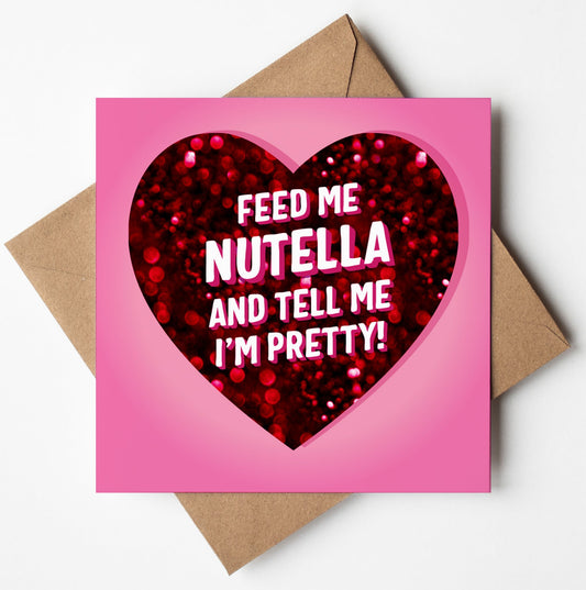 The "Feed Me Nutella And Tell Me I'm Pretty Love Card" is a pink Valentine's Day card adorned with a heart design and red glitter in the center. Inside, it humorously reads, "Feed me Nutella and tell me I'm pretty!" This amusing card comes with a brown envelope, perfect for bringing joy.