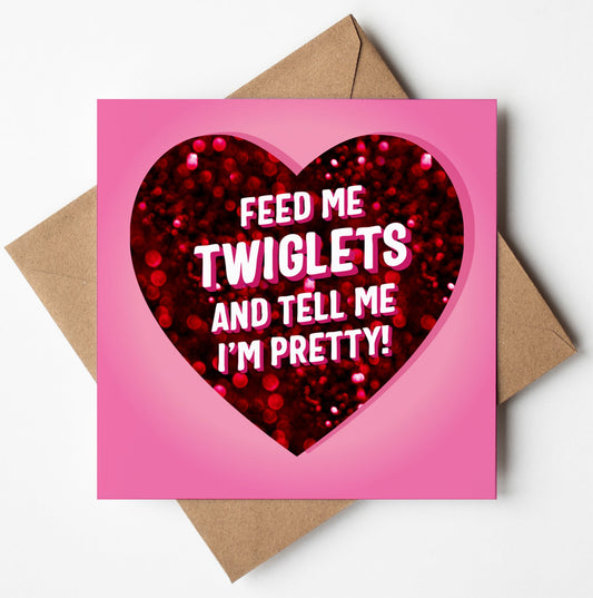 The Feed Me Twiglets And Tell Me I'm Pretty Love Card features a candy-colored design with a pink background and a red glittery heart, making it an ideal choice for a humorous anniversary card. Inside the heart, it reads, "Feed me Twiglets and tell me I'm pretty." The card comes attractively presented on a brown envelope.