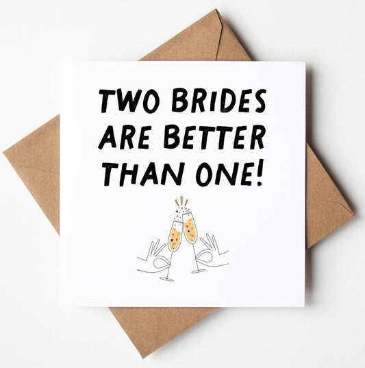 The "Two Brides Are Better Than One!" Gay Wedding Card is beautifully designed with the phrase above illustrated clinking champagne glasses. It comes with a brown envelope, set against a white backdrop, and is carefully packaged in a biodegradable bag. The inside of the card is left blank for your personal message.