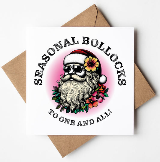 The "Sunglass Santa's Seasonal Bollocks To One And All! Xmas Card" features a humorous illustration of Santa Claus wearing sunglasses and a Santa hat, encircled by flowers. The card is emblazoned with the phrase "Seasonal Bollocks" above and "To One and All!" below. This adult Christmas card rests on a brown envelope, offering a witty twist to the classic seasonal greeting.