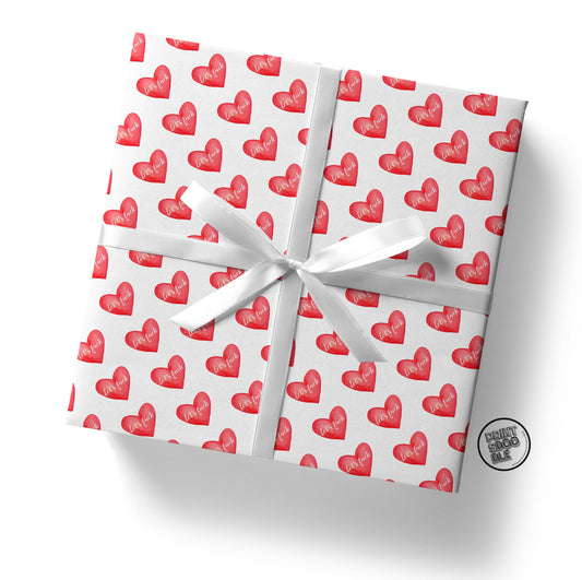 The "Let's Fuck Gift Wrap (Folded Sheet)" is an ideal choice for a Valentine's gift. This square gift box is wrapped in white paper adorned with red heart patterns, each heart highlighting the word "LOVE" in white. The finishing touch is a white ribbon bow, reflecting sophisticated gift wrap finesse.