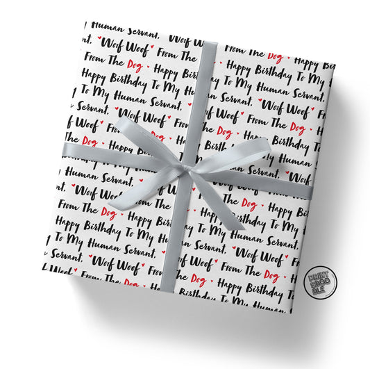 A birthday surprise for a Dog Mum comes wrapped in the "Human Dog Servant Birthday Gift Wrap," featuring playful dog-themed paper with black and red text that reads, "Happy Birthday to My Human Servant! Woof Woof! From The Dog." It's tied with a silver ribbon and adorned with a small round "DRUNK DOG BOX" logo.